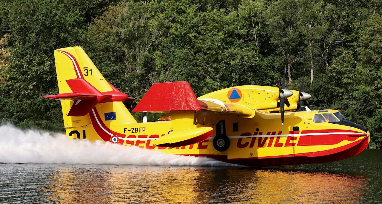 default-386 The yellow and red aircraft scoops up water while flying over the river.
