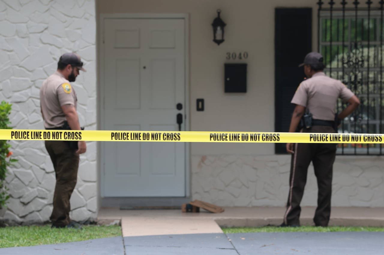 Police presence outside a door with caution tape reading: Police Line do not cross