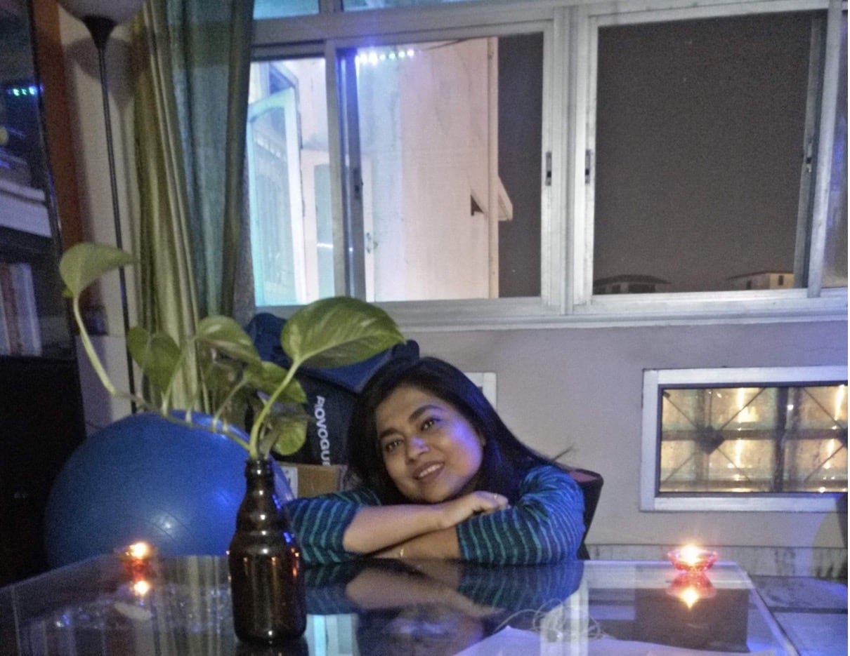 A woman sitting at a clear kitchen table, with large windows in the background.
