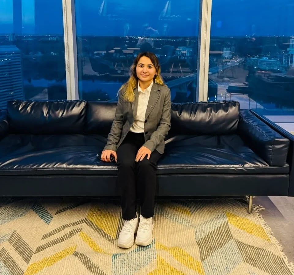 Farkhunda Hashimy sits on a black leather couch at the Nutrien Saskatoon Corporate Office. Saskatoon's dark skyline can be seen through the mirror behind her.